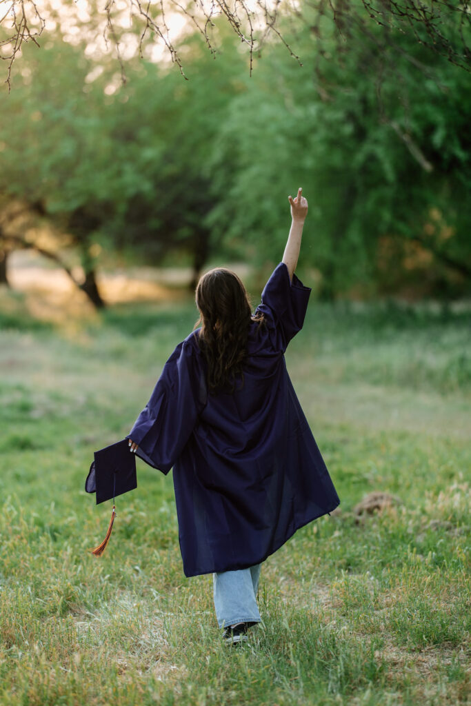 Senior photo with cap and gown in the green grass and trees at Butcher Jones Recreation Site, Salt River, Mesa, Arizona.